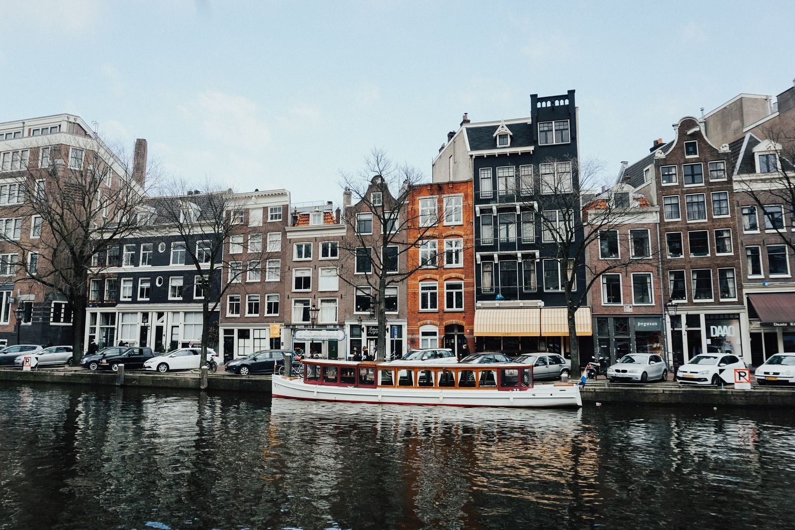 Boat cruising an Amsterdam canal between classic Dutch houses