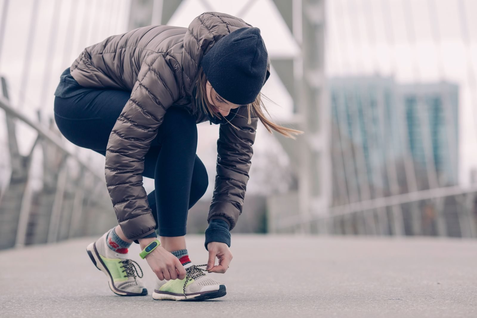 Corredora atándose las zapatillas en un puente antes de correr en invierno, regalos para runners