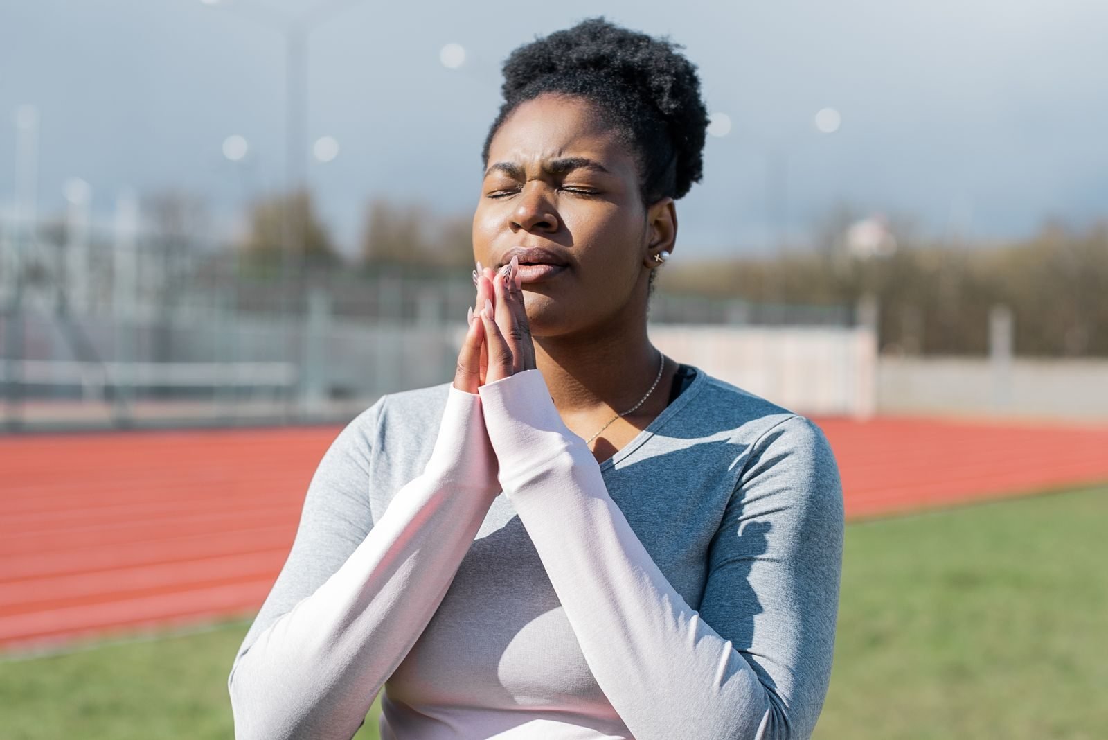 Woman with eyes closed practising how to breathe when running beside an athletics track