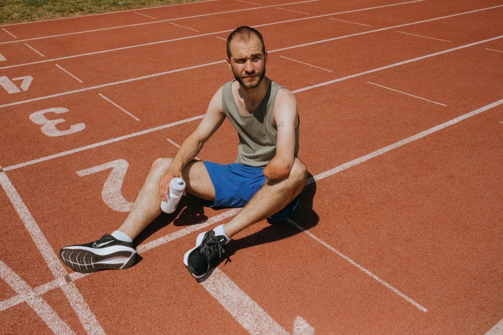 Atleta descansando sentado en una pista con una botella de agua, parte de la recuperación después de un maratón