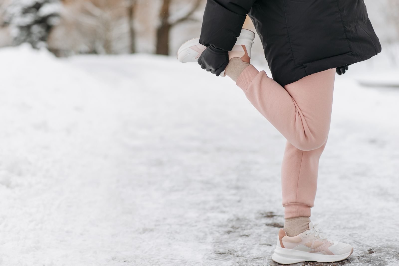 Corredora estirando en la nieve con ropa de invierno