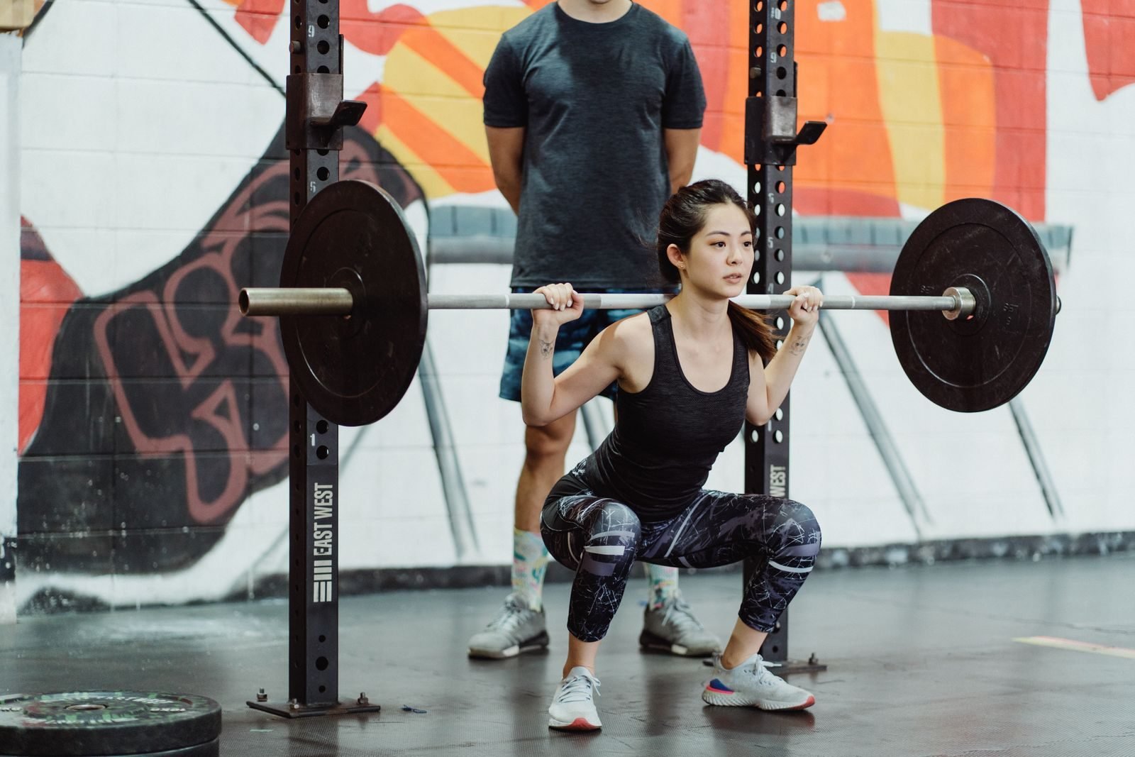 Mujer haciendo sentadillas con barra guiada por un entrenador para prevenir lesiones