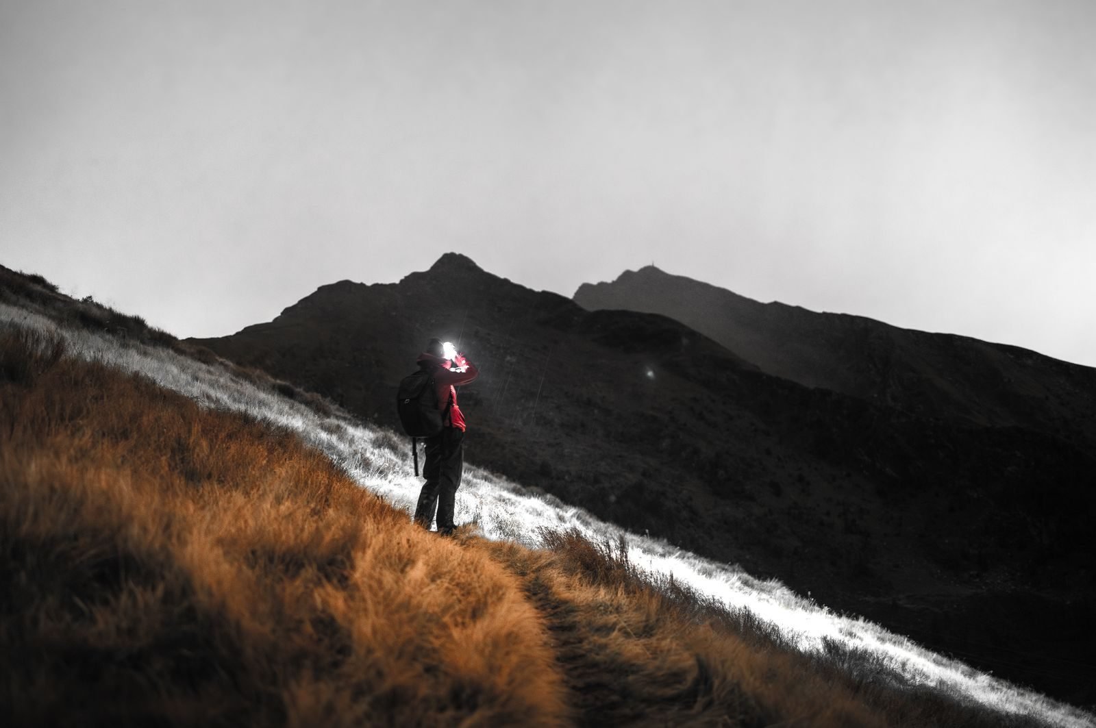 Person with a lit head torch walking along a mountain ridge at night