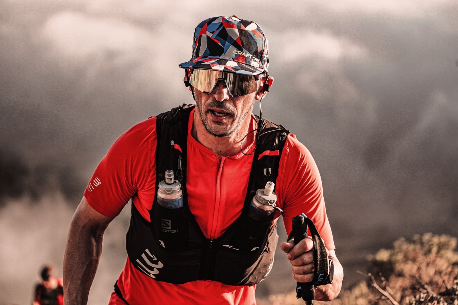 Corredor con chaleco de hidratación y bastones en una primera carrera de trail por terreno rocoso