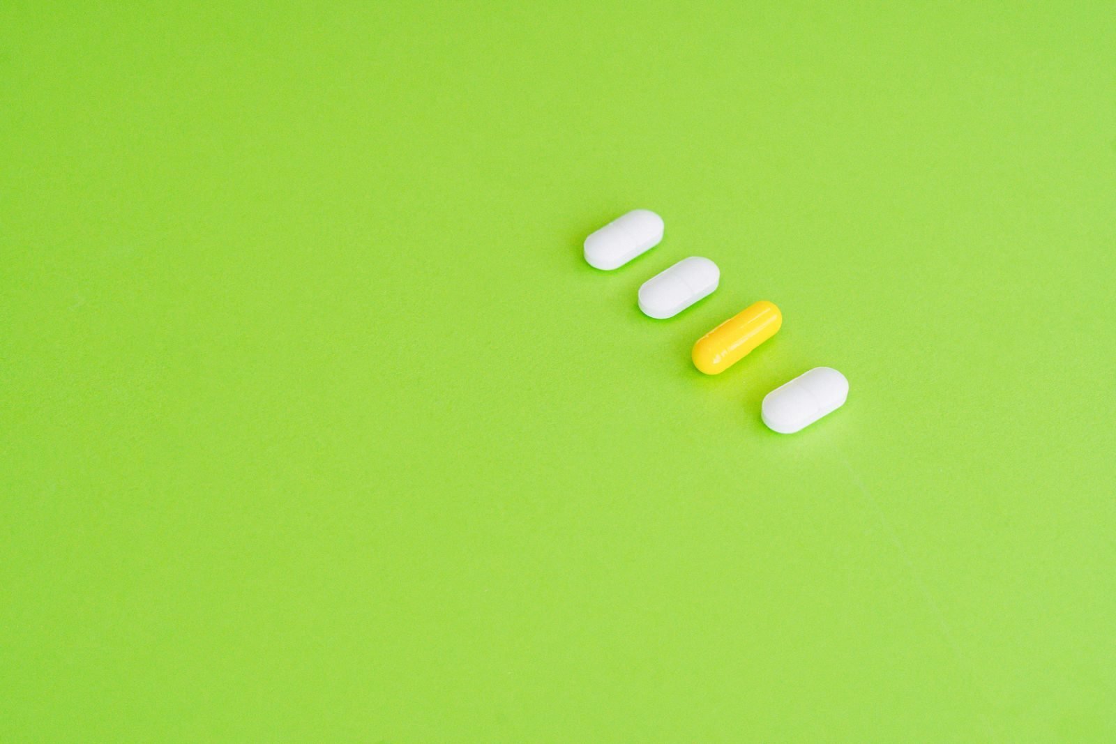 Fila de pastillas blancas y una amarilla sobre fondo verde