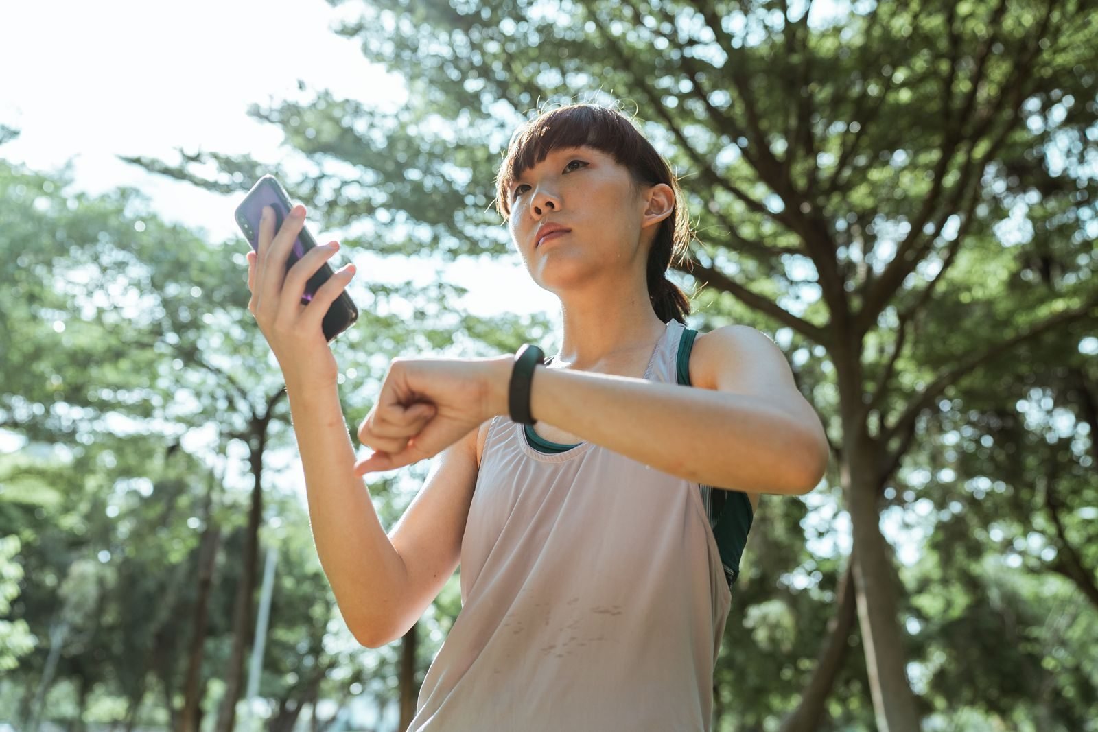 Woman in a park checking her watch and phone to plan how many days a week to run