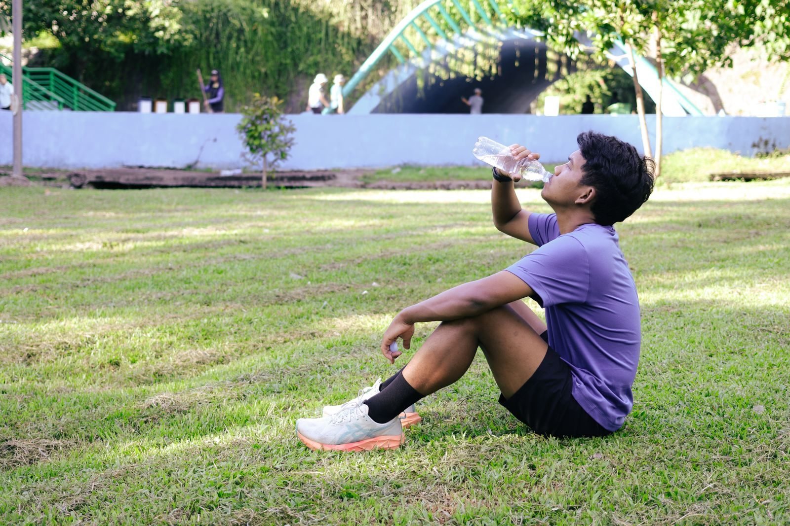 Young man resting on the grass and drinking water after a run