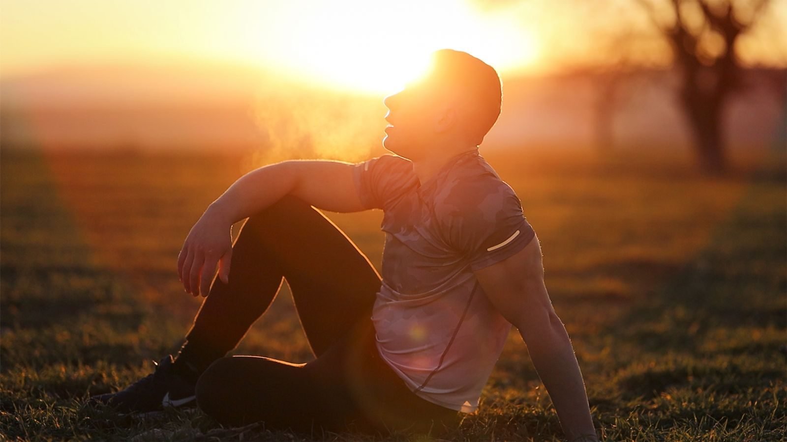 Hombre sentado en el campo al atardecer recuperando el aliento tras correr