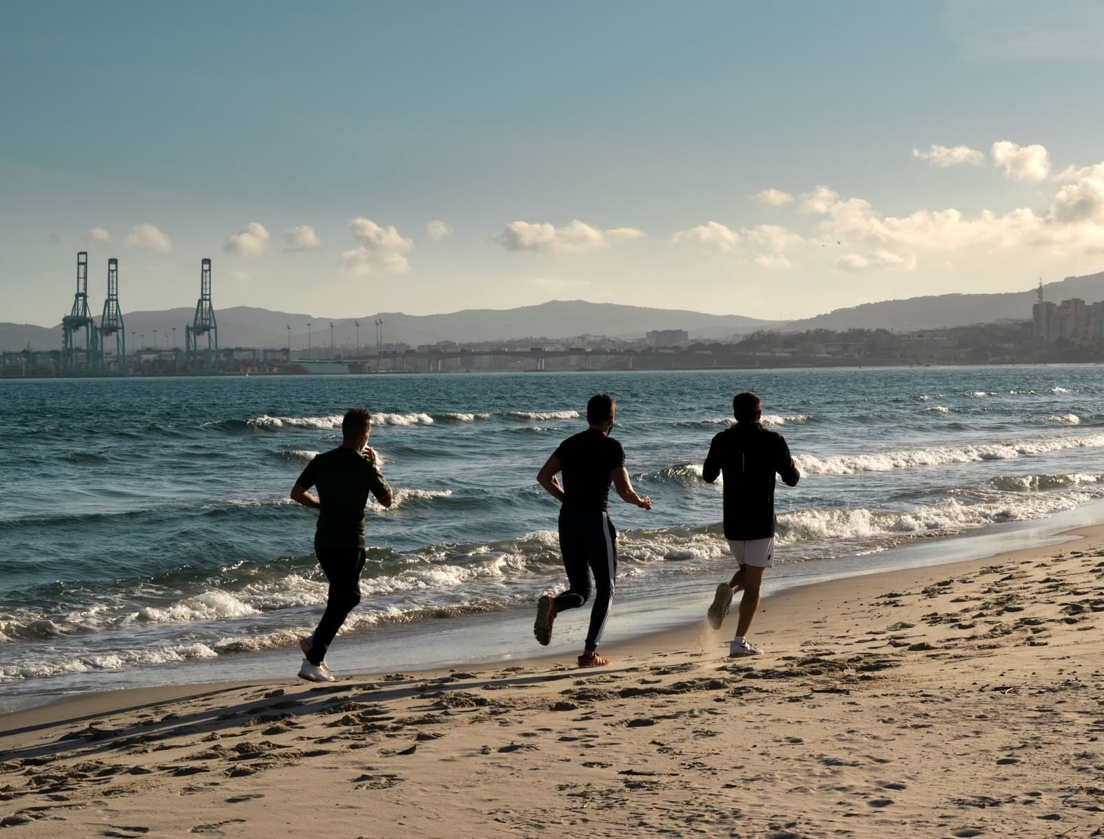 Three runners jogging along the shoreline of a beach