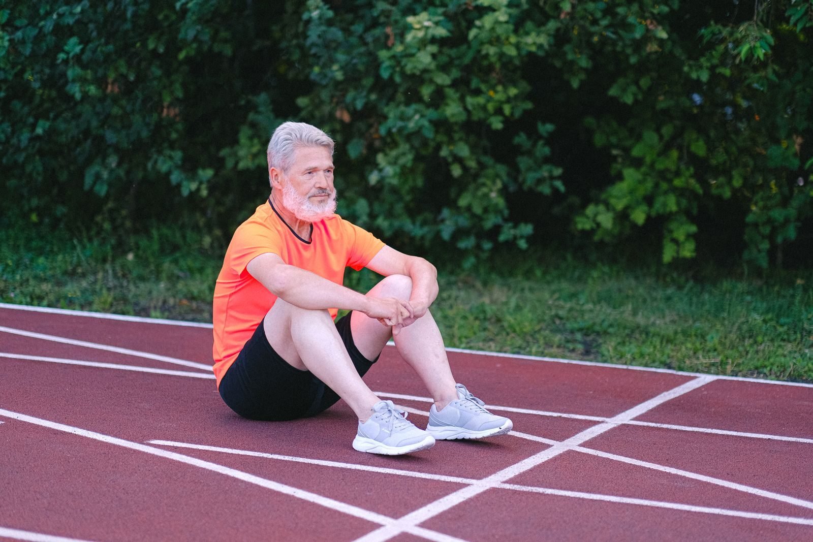 Hombre mayor sentado en la pista mirando al horizonte, cansado tras entrenar