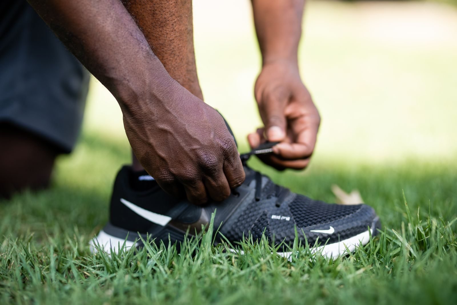 Person tying a black shoe on the grass, wearing socks and running clothes