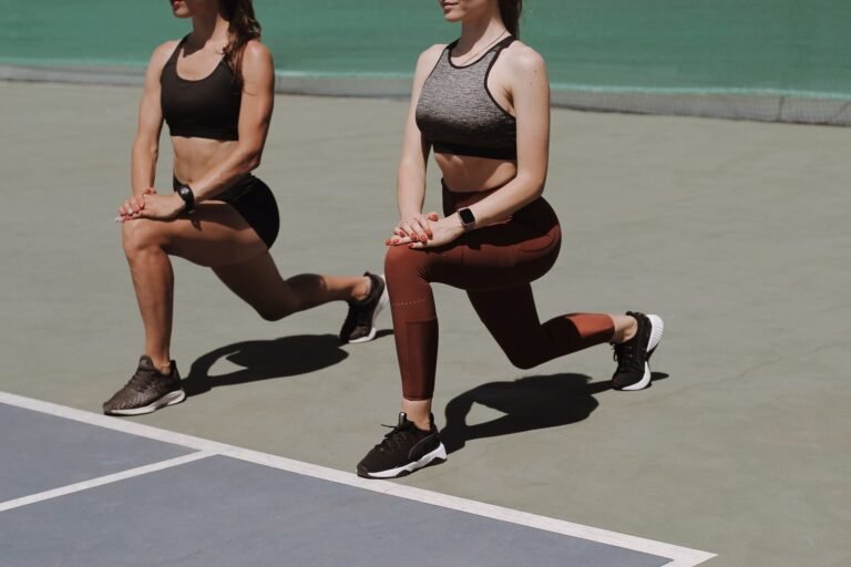 Two women doing lunges on a sports court as part of their strength training for runners