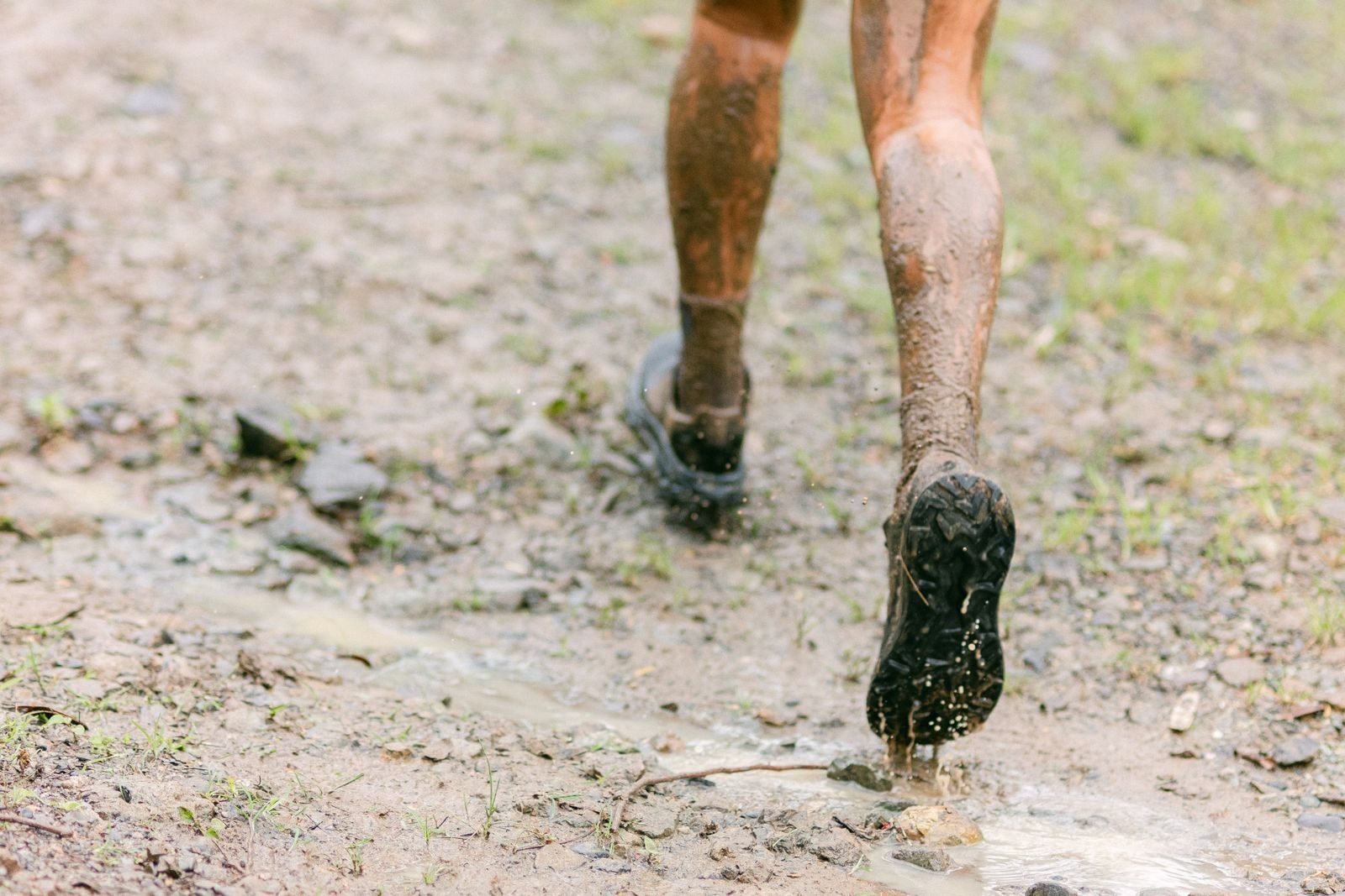Piernas y zapatillas de trail manchadas de barro corriendo por un sendero húmedo
