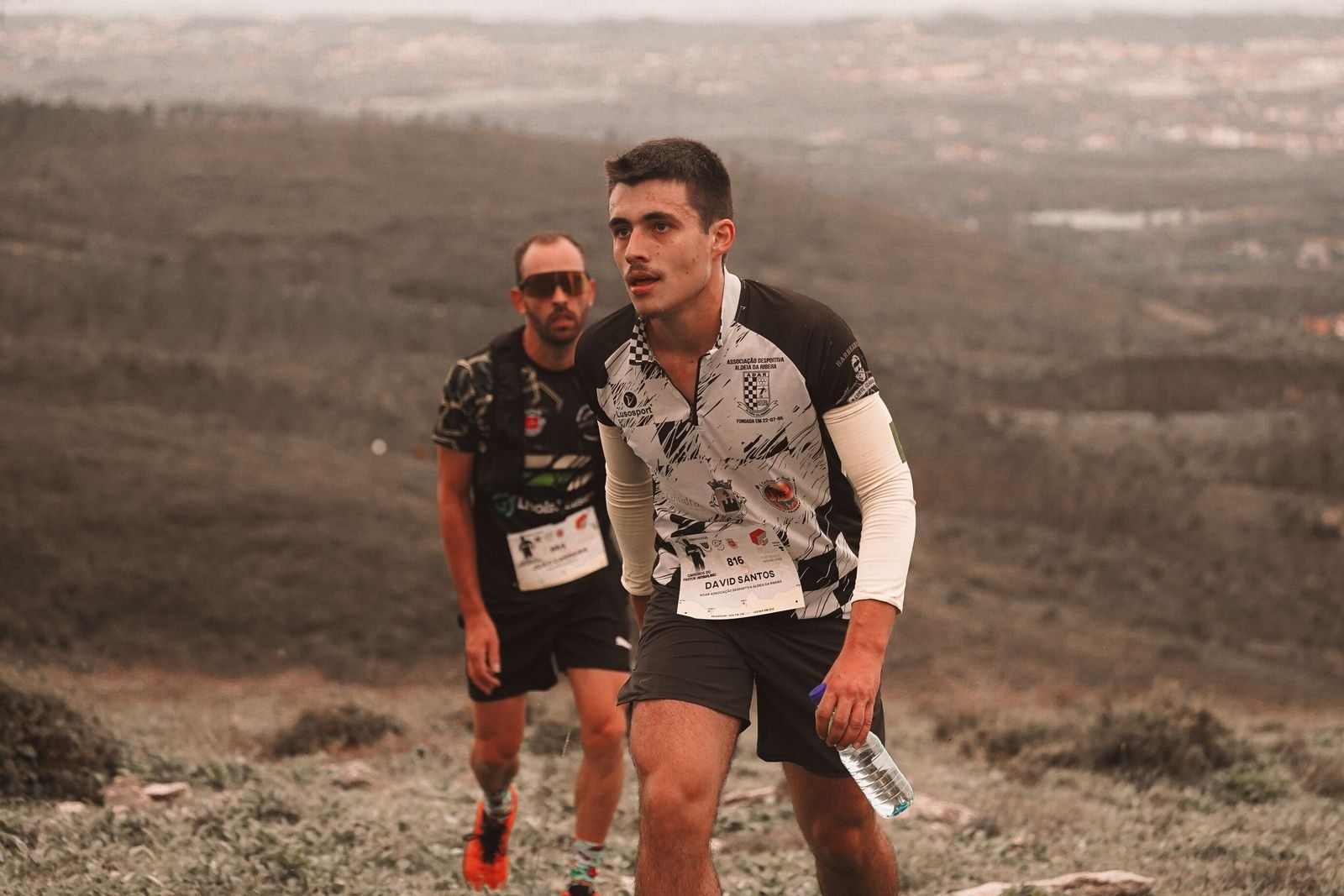 Two trail runners climbing a hillside during a race