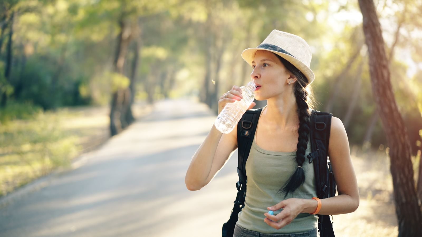 Hiker drinking water on a forest trail, part of trail race mandatory gear