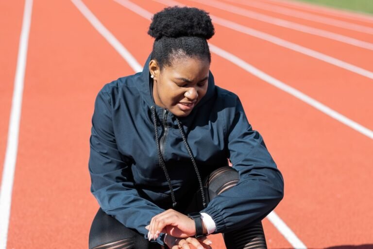 Runner on an athletics track checking her pace on a GPS watch