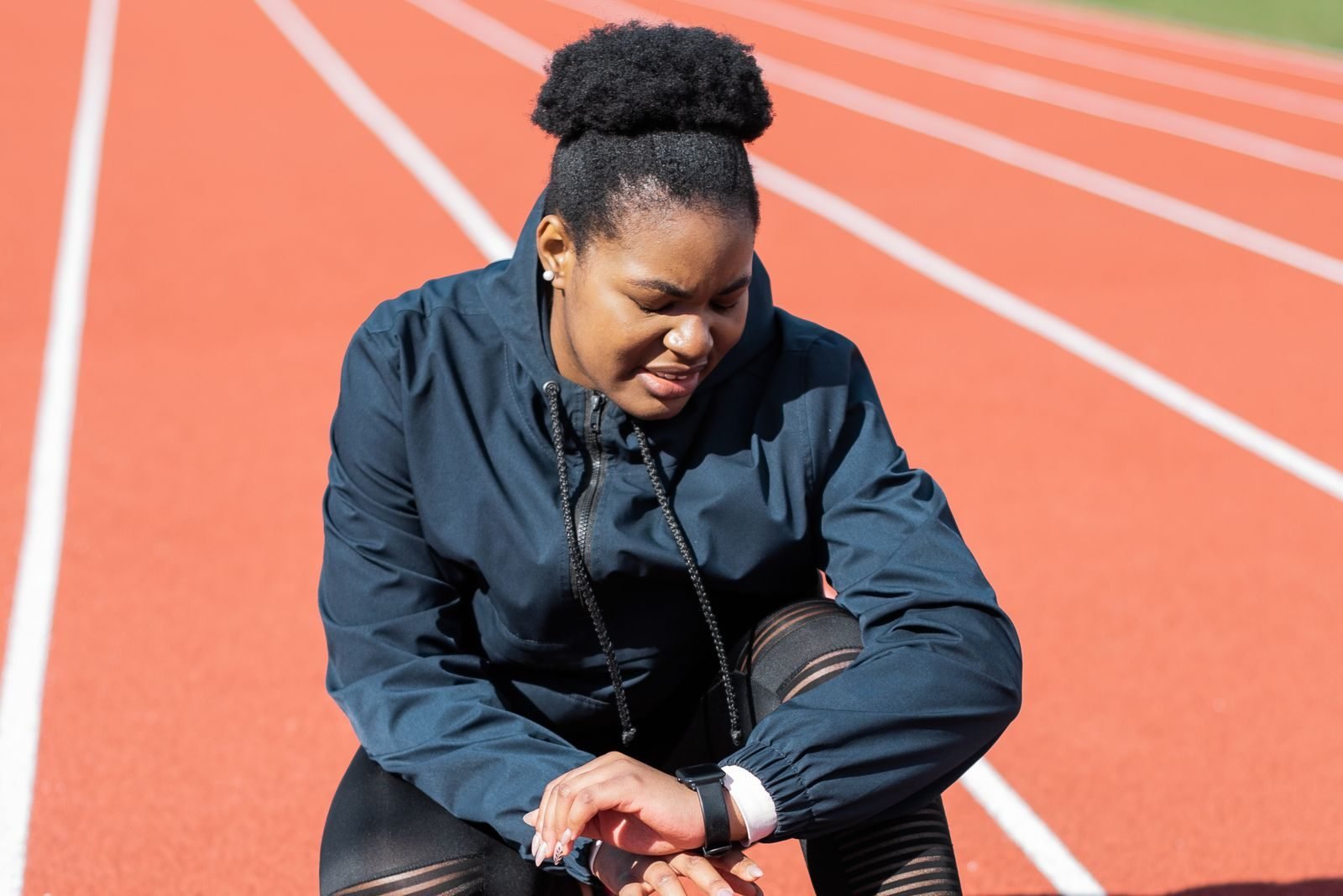 Runner on an athletics track checking her pace on a GPS watch