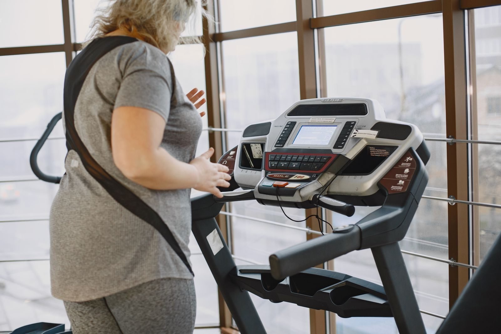 Woman next to a treadmill in a gym with large windows