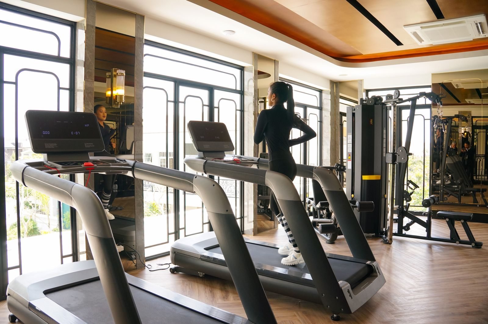 Woman running on a treadmill in a gym with large windows