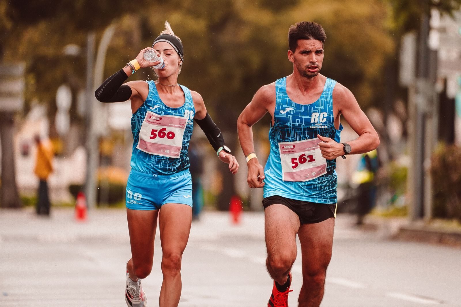 Two runners drinking water while running a road race